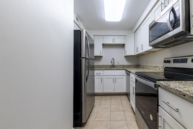 kitchen with light tile patterned floors, appliances with stainless steel finishes, light stone countertops, white cabinetry, and a sink