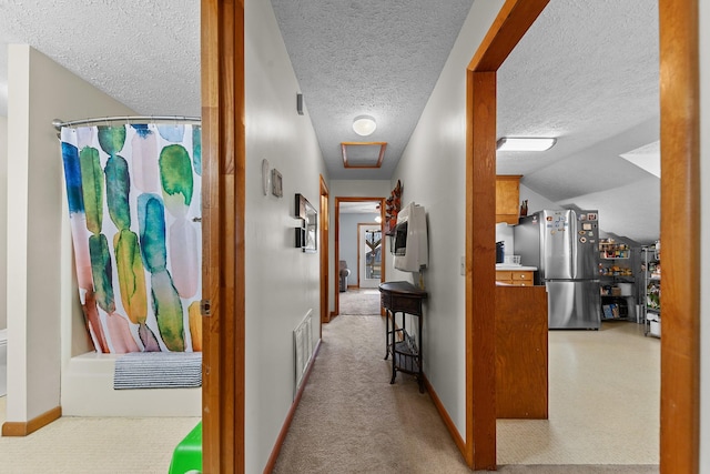 corridor with baseboards, visible vents, light colored carpet, vaulted ceiling, and a textured ceiling