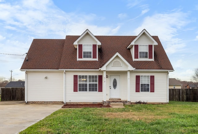 new england style home with roof with shingles, fence, driveway, and a front lawn