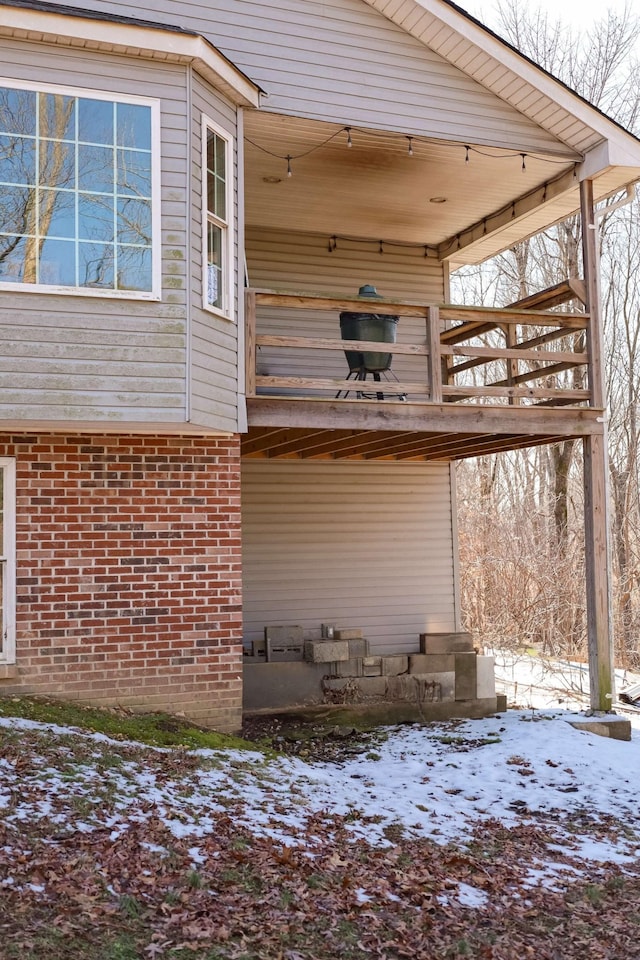 view of snowy exterior featuring brick siding and a deck