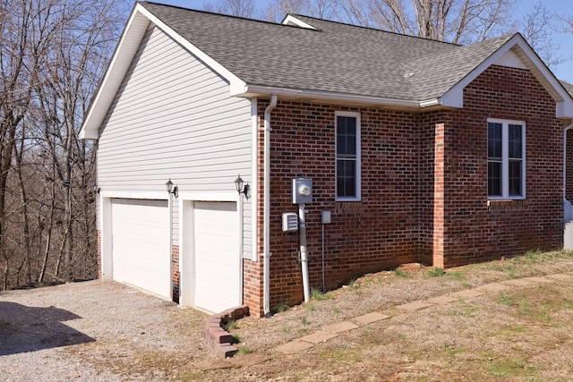 view of side of home featuring a garage, brick siding, roof with shingles, and gravel driveway