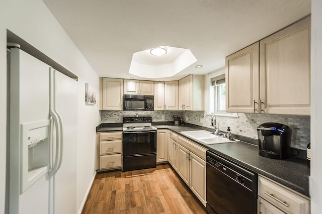 kitchen featuring light wood finished floors, dark countertops, backsplash, a sink, and black appliances