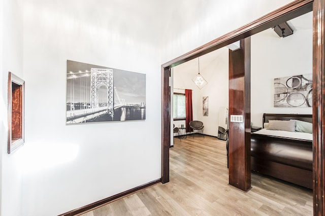 hallway with baseboards, a towering ceiling, and light wood finished floors