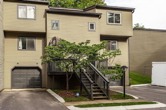 view of property with stairs, aphalt driveway, and a garage