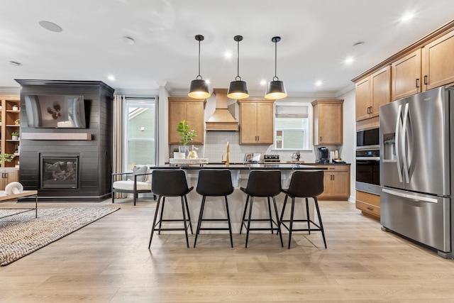 kitchen featuring a large fireplace, a kitchen island, hanging light fixtures, appliances with stainless steel finishes, and custom range hood