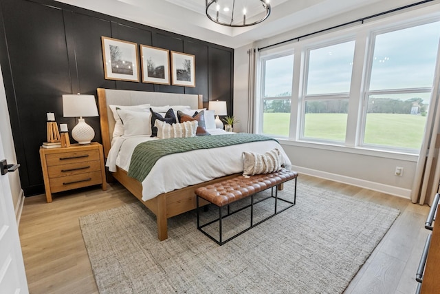 bedroom with light wood-style floors, a tray ceiling, baseboards, and a notable chandelier