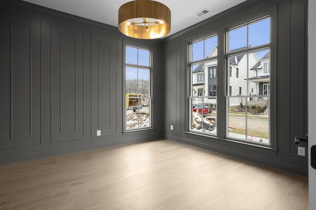 spare room with light wood-type flooring, visible vents, and a decorative wall