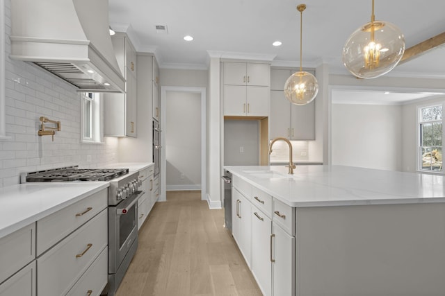 kitchen featuring a center island with sink, custom range hood, high end stove, pendant lighting, and a sink