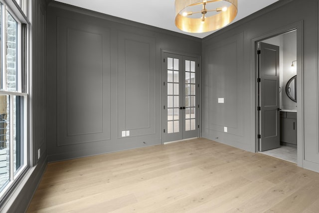 empty room featuring light wood-type flooring, french doors, a healthy amount of sunlight, and a decorative wall