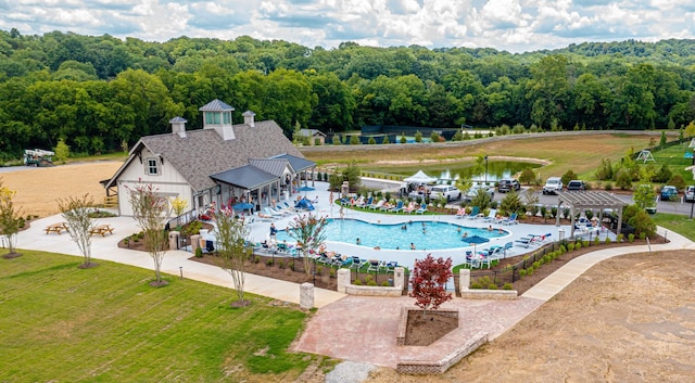 community pool featuring a patio area, a water view, fence, and a view of trees