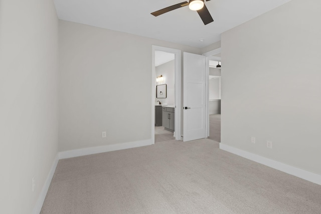 unfurnished bedroom featuring baseboards, ensuite bath, a ceiling fan, and light colored carpet