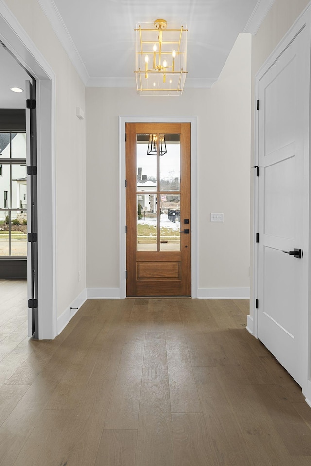 entrance foyer with ornamental molding, a notable chandelier, baseboards, and wood finished floors