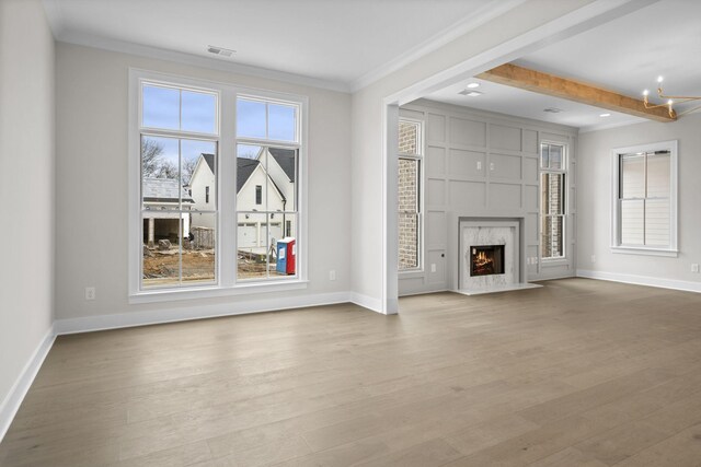 unfurnished living room with light wood-style floors, a wealth of natural light, ornamental molding, and a high end fireplace