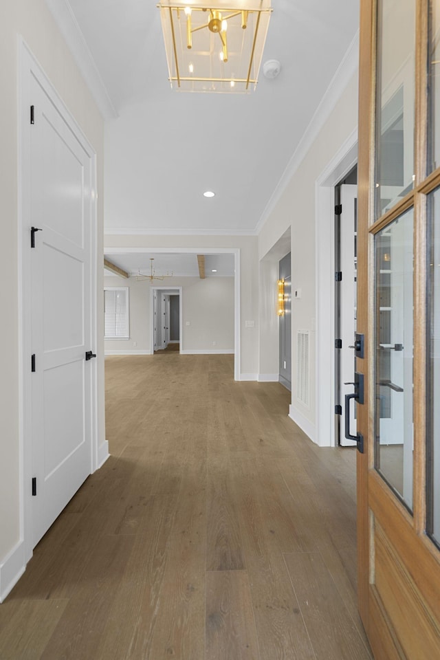 hall with baseboards, ornamental molding, a chandelier, and wood finished floors