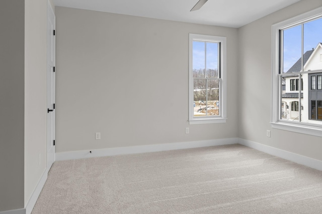 spare room with a ceiling fan, light colored carpet, and baseboards