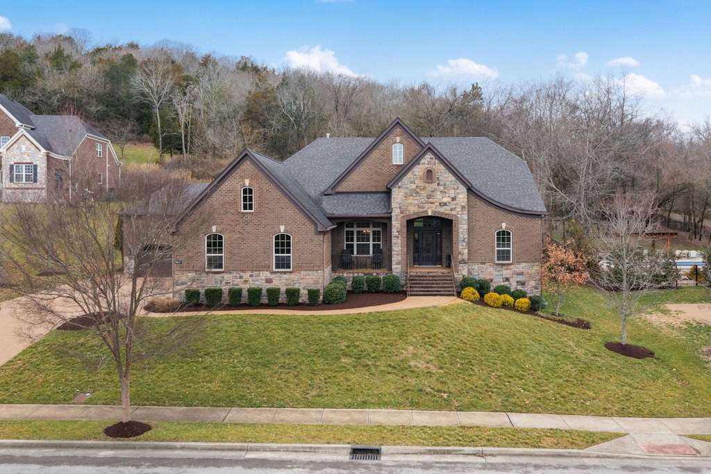 french provincial home featuring stone siding, a front lawn, and brick siding