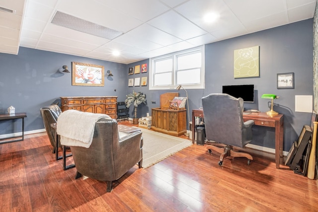 office space featuring a paneled ceiling, baseboards, visible vents, and hardwood / wood-style floors