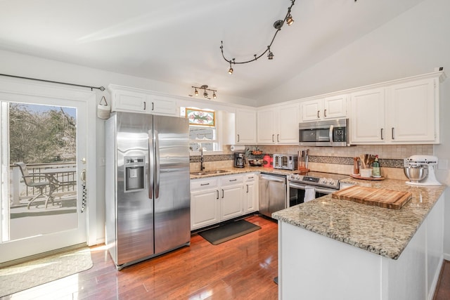 kitchen featuring stainless steel appliances, lofted ceiling, white cabinets, a sink, and a peninsula