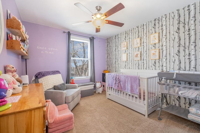 bedroom featuring a ceiling fan, a crib, light colored carpet, and wallpapered walls