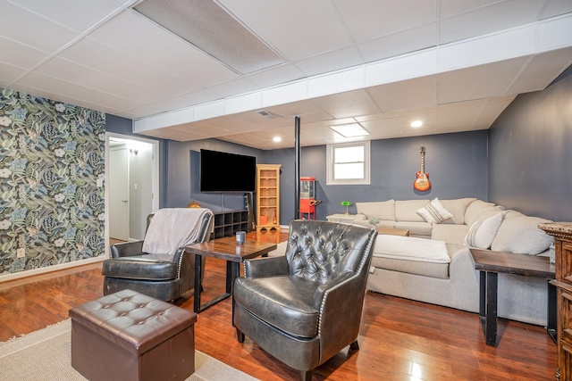 living area with a paneled ceiling, visible vents, wood finished floors, baseboards, and wallpapered walls