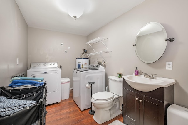 half bathroom featuring toilet, electric water heater, wood finished floors, vanity, and washer and clothes dryer