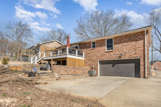 rear view of house with driveway, a garage, central AC unit, a wooden deck, and brick siding