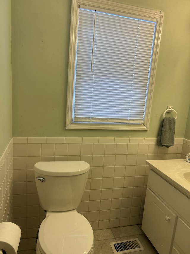 bathroom featuring visible vents, wainscoting, toilet, vanity, and tile walls