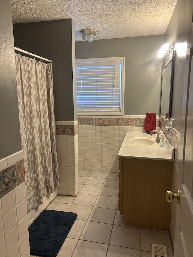 full bath with a textured ceiling, tile walls, vanity, visible vents, and tile patterned floors