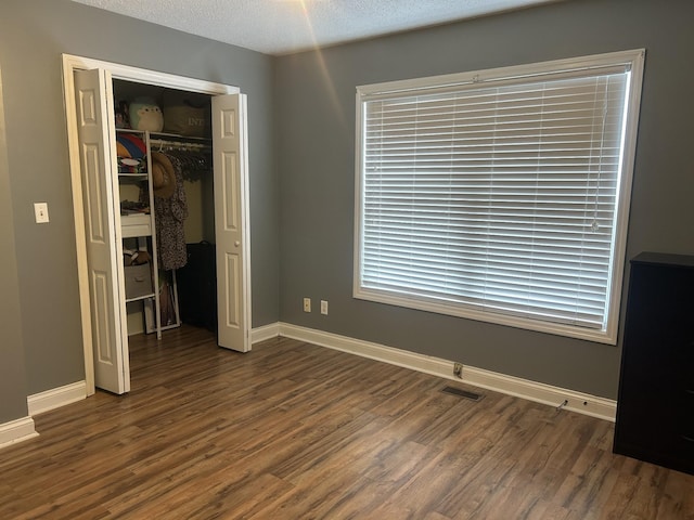 unfurnished bedroom featuring a textured ceiling, dark wood-style flooring, visible vents, baseboards, and a closet