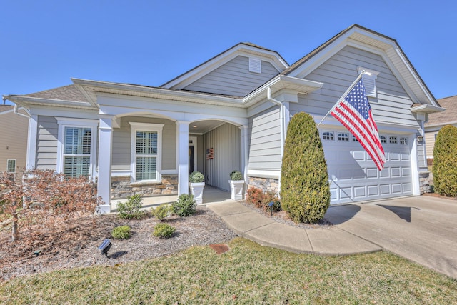 view of front facade with stone siding, a porch, an attached garage, and driveway