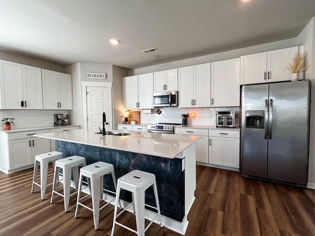 kitchen featuring a breakfast bar, a sink, white cabinetry, appliances with stainless steel finishes, and dark wood-style floors