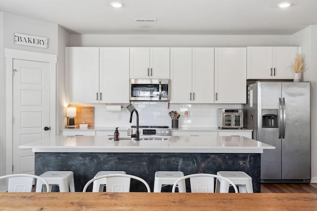 kitchen featuring stainless steel appliances, a kitchen bar, visible vents, and decorative backsplash