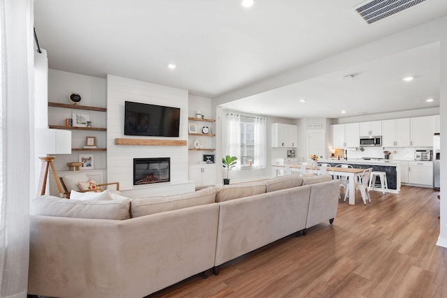 living room featuring recessed lighting, visible vents, a fireplace, and light wood-style flooring