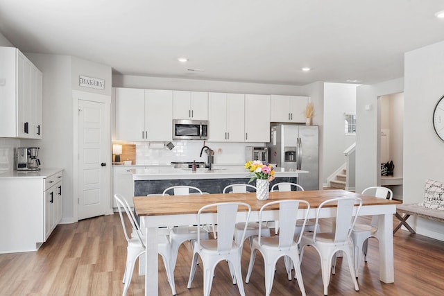 kitchen featuring stainless steel appliances, backsplash, light wood-style flooring, a kitchen island with sink, and a sink