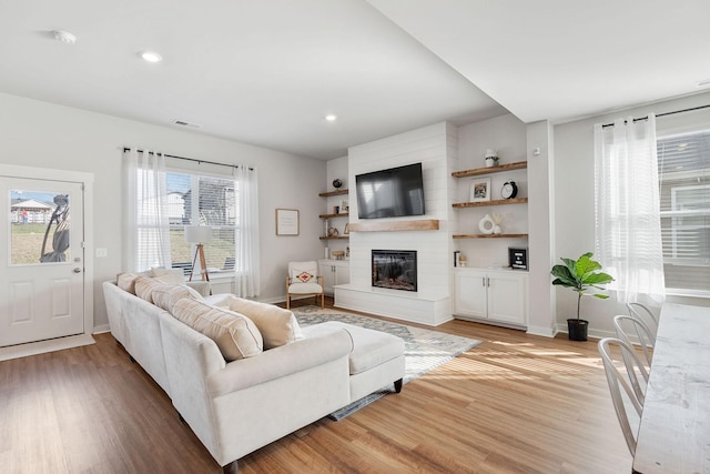 living area featuring recessed lighting, baseboards, a fireplace, and light wood finished floors