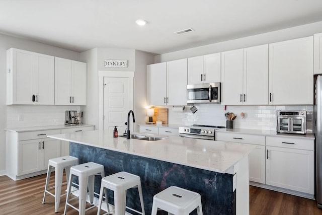 kitchen with dark wood-type flooring, a breakfast bar, a sink, visible vents, and appliances with stainless steel finishes