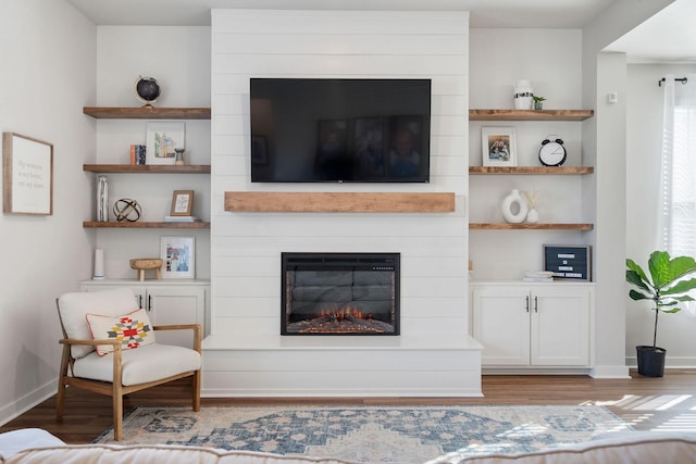 living area featuring built in shelves, a fireplace, wood finished floors, and baseboards