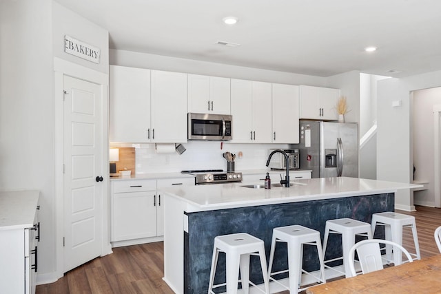 kitchen with a sink, white cabinetry, appliances with stainless steel finishes, backsplash, and a kitchen bar