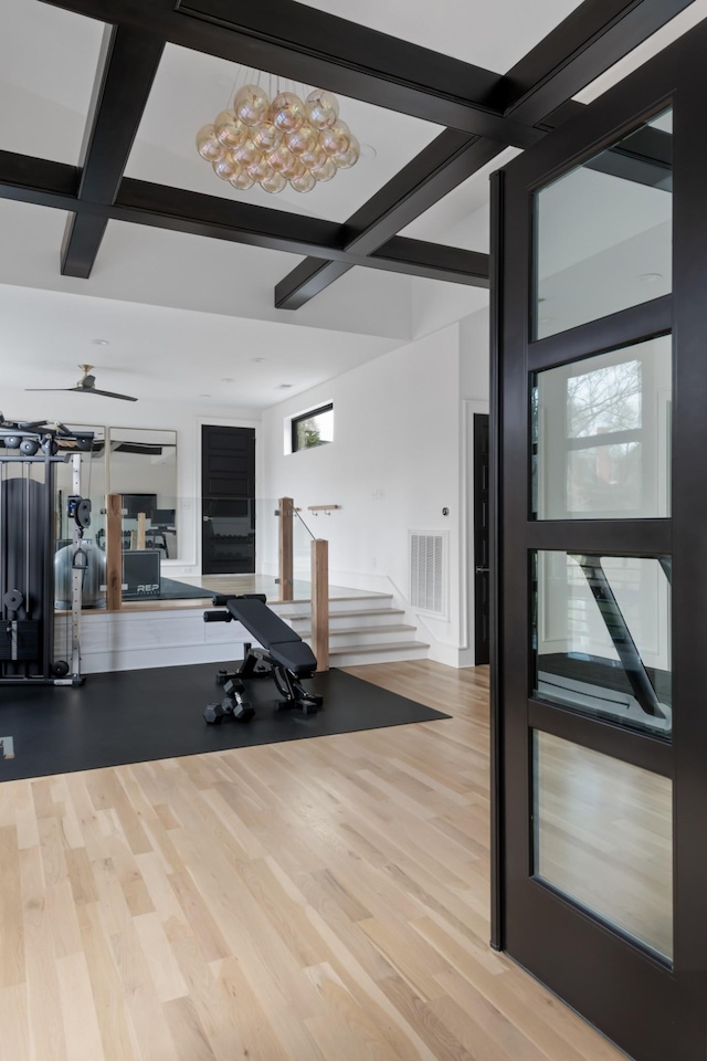 workout area with light wood-type flooring, ceiling fan, visible vents, and coffered ceiling