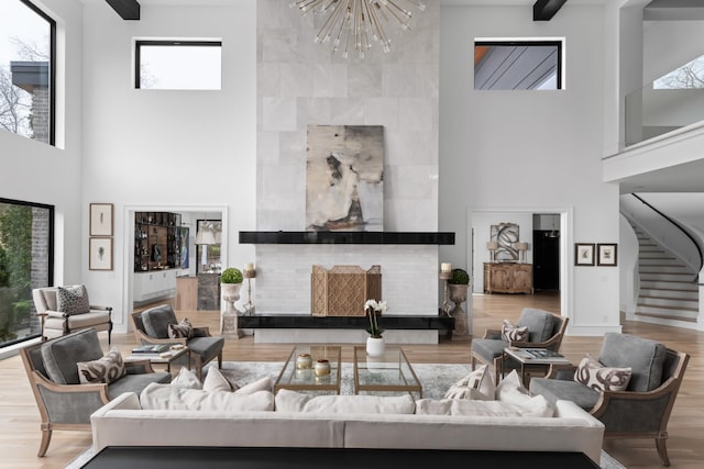 living room featuring a notable chandelier, wood finished floors, a towering ceiling, stairs, and a tiled fireplace