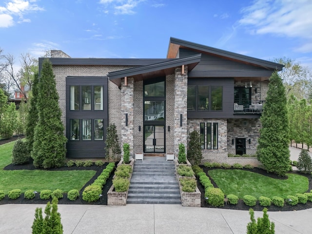 contemporary house featuring a balcony, a chimney, a front lawn, and brick siding