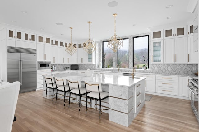 kitchen with high end appliances, pendant lighting, glass insert cabinets, and a center island with sink