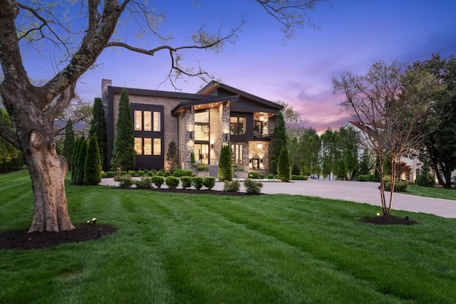 modern home with stone siding, a chimney, and a front yard