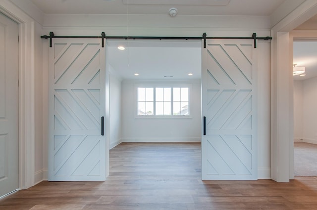 unfurnished room with light wood-style floors, a barn door, and baseboards