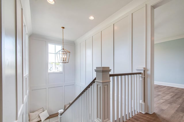 corridor with a chandelier, a decorative wall, crown molding, and an upstairs landing