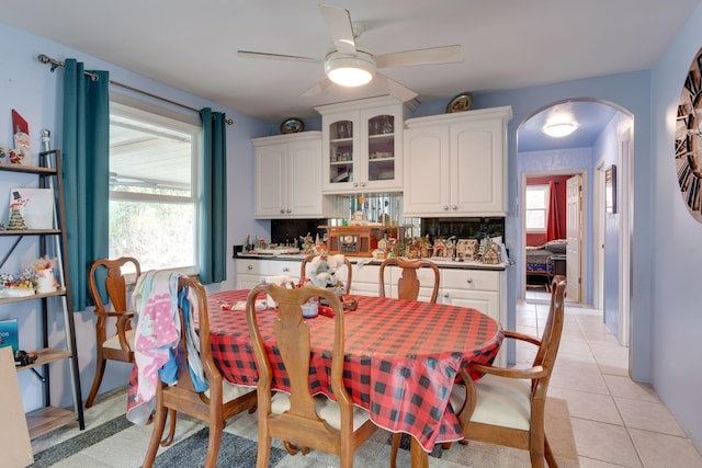 dining area featuring ceiling fan, arched walkways, and light tile patterned flooring