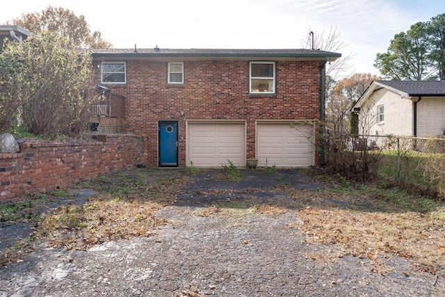 rear view of house featuring a garage, brick siding, fence, and driveway