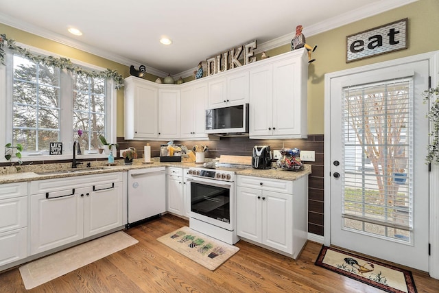 kitchen featuring crown molding, light wood-style floors, white cabinets, a sink, and white appliances