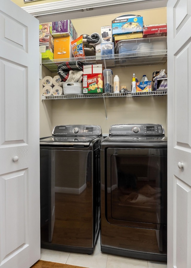 clothes washing area featuring laundry area, light tile patterned flooring, and washing machine and clothes dryer