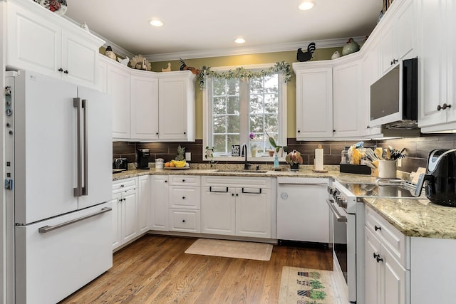 kitchen featuring white appliances, wood finished floors, a sink, white cabinetry, and crown molding